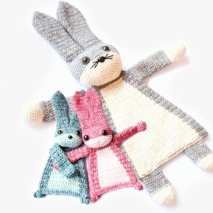 May include: Three crocheted bunny plushies. The largest bunny is gray and white, and the two smaller bunnies are teal and pink.
