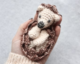 May include: A crocheted hedgehog toy with brown and beige yarn. The hedgehog is curled up in a ball with its eyes closed.