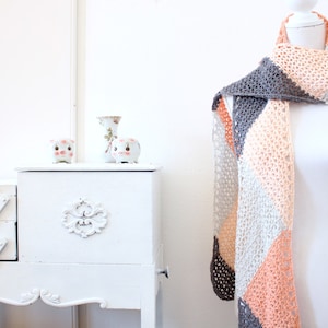 May include: A crocheted scarf with a gray, white, and peach color pattern. The scarf is draped over a white mannequin.