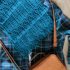 May include: A blue plaid shirt with a teal crocheted scarf and a brown leather crossbody bag.