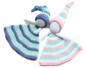 May include: Two crocheted dolls with striped dresses and hats. One doll has a blue, gray, and green dress and hat, while the other has a pink, white, and green dress and hat.
