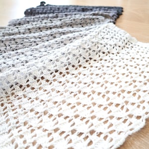 Puede incluir: Un conjunto de manteles individuales de ganchillo en varios tonos de gris, de oscuro a claro, con un mantel individual blanco en la parte inferior.