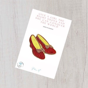 May include: Red glitter ruby slippers pin with a quote by Marilyn Monroe: "Give a girl the right shoes and she can conquer the world."