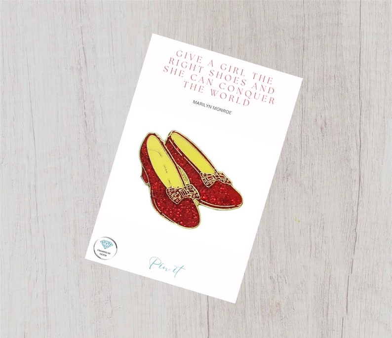 May include: Red glitter ruby slippers pin with a quote by Marilyn Monroe: "Give a girl the right shoes and she can conquer the world."