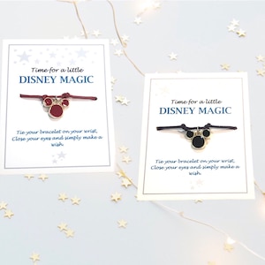Könnte beinhalten: Zwei Karten mit dem Text "Time for a little DISNEY MAGIC" und Anweisungen, das Armband um dein Handgelenk zu binden, die Augen zu schließen und einen Wunsch zu machen. Jede Karte hat ein Armband aus Schnur mit einem Mickey-Maus-Anhänger. Ein Anhänger ist rot und der andere ist schwarz.