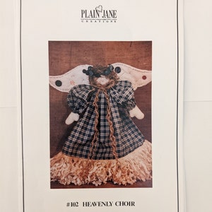 May include: A sewing pattern for a rag doll angel with a plaid dress, a brown yarn halo, and a fringe skirt. The pattern is titled "#102 HEAVENLY CHOIR" and is from Plain Jane Creations.