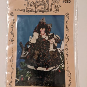 May include: A sewing pattern for a rag doll with a red and white checkered dress and a white cat. The pattern is titled "Strawberry and Little Patch" and is from Sweet Sugar Ragtown #380.