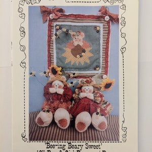 May include: Sewing pattern for a 10-inch boy and girl bear with bees. The pattern includes a 11-inch by 11-inch wallhanging. The pattern is titled 'Bee-ing Beary Sweet' and is pattern number 138.