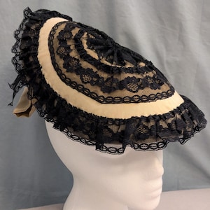 May include: A beige and black lace hat with a wide brim. The hat is trimmed with black lace and has a ruffled edge.