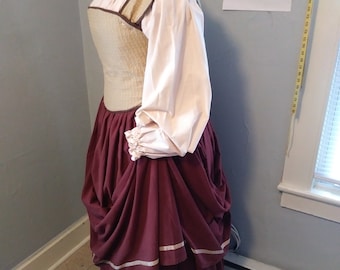 May include: A brown and beige bodice with a white blouse and a burgundy skirt with white trim. The skirt is gathered and has a layered look.
