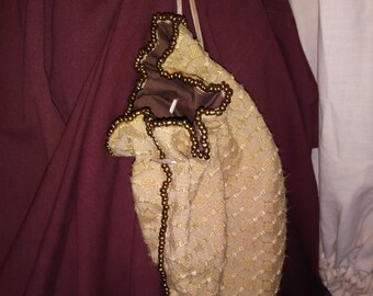 May include: A beige fabric drawstring bag with a brown lining and gold bead trim. The bag is hanging from a white cord.
