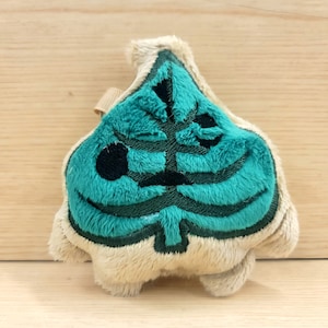 May include: A plush toy shaped like a green leaf with a black outline. The leaf is a popular symbol from the video game Animal Crossing.