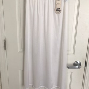 May include: White anti-cling slip skirt with a lace trim. The skirt is hanging on a hanger and has a tag that says "Anti-Cling" and "Antron® Nylon".