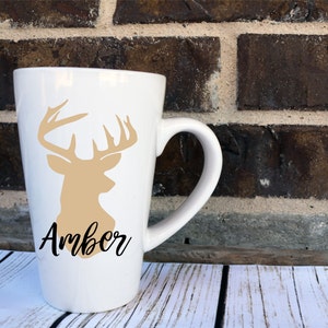 May include: White ceramic mug with a tan deer silhouette and the name "Amber" in black script.