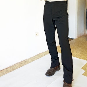May include: A light beige long-sleeved shirt with a subtle geometric pattern and a mandarin collar, paired with solid black trousers. The shirt features a button-down front and long sleeves with cuffs, while the trousers have a straight-leg cut.