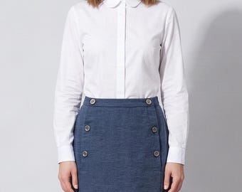 May include: A crisp white long-sleeved button-down shirt with a rounded Peter Pan collar, paired with a high-waisted blue skirt featuring two vertical rows of four circular buttons each, creating a structured and clean aesthetic for daily wear.