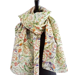 Puede incluir: Una bufanda de seda blanca con un patrón floral con flores y enredaderas verdes, rojas y moradas. La bufanda está drapeada sobre un maniquí.