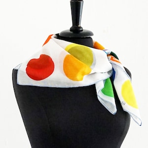 May include: White silk scarf with a colorful polka dot pattern. The dots are red, yellow, green, and blue. The scarf is tied around a black mannequin's neck.