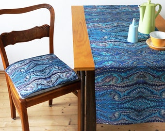Könnte beinhalten: Ein Holzstuhl mit einem blauen und weißen gemusterten Kissen steht neben einem Holztisch mit einem blauen und weißen gemusterten Tischläufer.