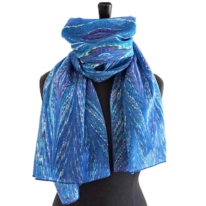 Könnte beinhalten: Blauer Schal mit Marmormuster, präsentiert auf einer schwarzen Schaufensterpuppe. Der Schal weist Blautöne, Weiß und einen Hauch von Lila und Rosa auf. Der Stoff wirkt leicht und fließend, mit einem detaillierten, wellenartigen Design.