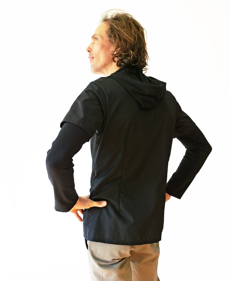 Puede incluir: Una camiseta negra de manga corta con capucha superpuesta sobre una capa base negra de manga larga. La prenda presenta una capucha en el cuello y una confecci&oacute;n en tejido negro liso y s&oacute;lido. Se lleva puesta con pantalones de color claro.