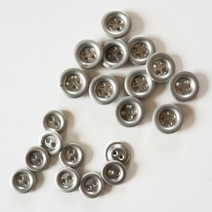 Peut inclure: Un ensemble de boutons en métal argenté, chacun avec cinq trous. Les boutons sont disposés en forme de triangle avec un petit groupe de boutons en dessous.