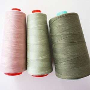 Könnte beinhalten: Drei Garnrollen, eine rosa, eine grün und eine olivgrün.