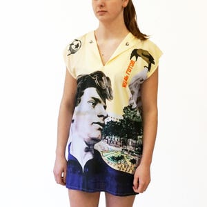 May include: A sleeveless, collared dress with a V-neck. The dress features a portrait of a man with goggles, a landscape scene, and the text "будь готов" in red. The top is light yellow, and the bottom is navy blue.