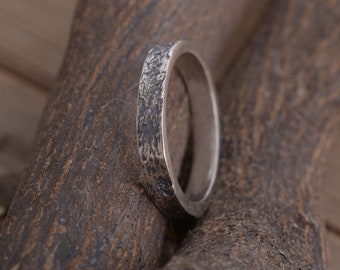 May include: A silver band ring with a textured finish. The ring is thick and has a rounded shape.