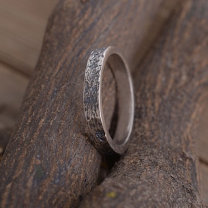 Op de afbeelding: Een zilveren bandring met een getextureerde afwerking. De ring is dik en heeft een afgeronde vorm.