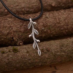 Könnte beinhalten: Eine silberne Halskette mit einem zarten Zweig-Anhänger. Der Anhänger zeigt einen langen, schlanken Zweig mit kleinen Blättern und Knospen. Die Halskette ist an einem schwarzen Lederband.