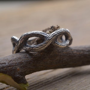 Puede incluir: Un anillo de plata con un diseño de rama retorcida. El anillo está hecho para parecer un trozo de madera natural.