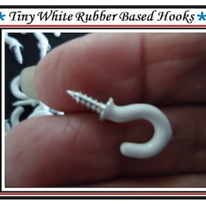 May include: A close-up of a white rubber-based hook with a screw. The hook is held in a hand. The hook is small and has a simple design.