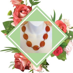 May include: A necklace made with carnelian gemstone beads. The beads are a deep orange color and are oval shaped. The necklace is on a white mannequin.