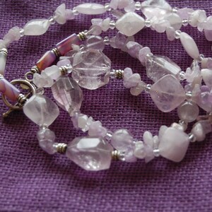 May include: A multi-strand necklace made with light purple and clear faceted gemstone beads. The necklace has a silver clasp and is strung on silver wire.