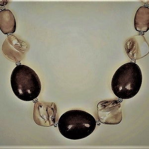 May include: A necklace made of brown and white oval and square shaped beads. The beads are strung on a silver chain.