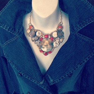 May include: A statement necklace made of various materials, including shells, buttons, and beads. The necklace is a mix of gold, white, and red colors.