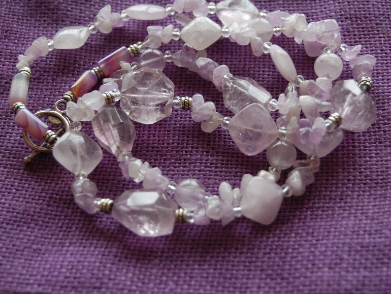 May include: A multi-strand necklace made with light purple and clear faceted gemstone beads. The necklace has a silver clasp and is strung on silver wire.