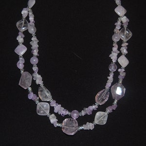 May include: A double-strand necklace made with light purple amethyst and clear quartz beads. The necklace features a variety of shapes and sizes of beads, including round, oval, and rectangular.