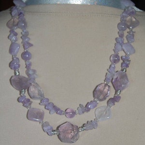May include: A double-strand necklace made of lavender amethyst and clear quartz beads. The necklace features a variety of shapes and sizes of beads, including round, oval, and irregular shapes.