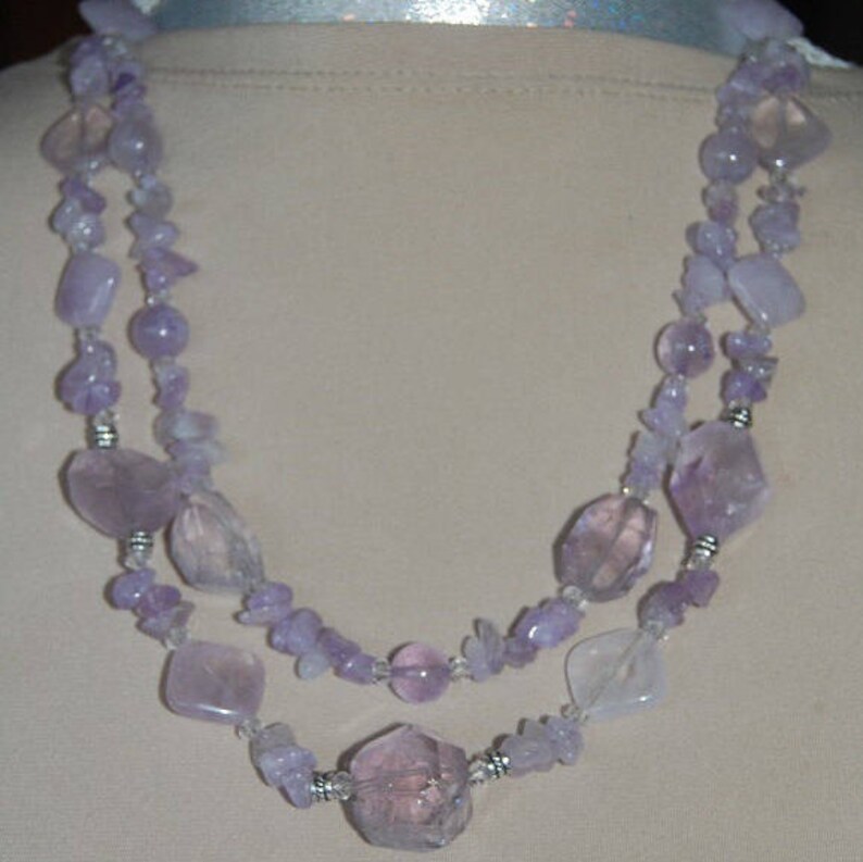 May include: A double-strand necklace made of lavender amethyst and clear quartz beads. The necklace features a variety of shapes and sizes of beads, including round, oval, and irregular shapes.