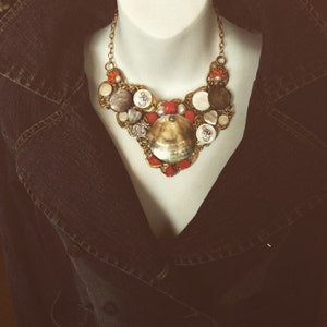 May include: A gold necklace with a variety of shells, beads, and charms. The necklace is on a white mannequin and has a vintage feel.