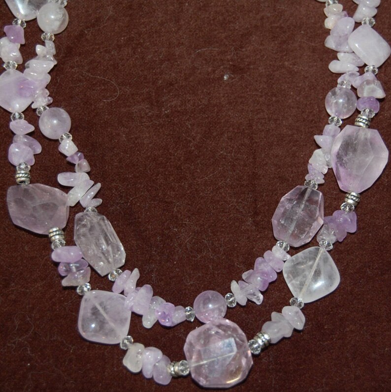 May include: A double-strand necklace made of light purple and clear faceted gemstone beads. The necklace is made of various shapes and sizes of beads.