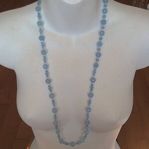 May include: A light blue beaded necklace with a variety of shades of blue beads. The necklace is on a white mannequin.