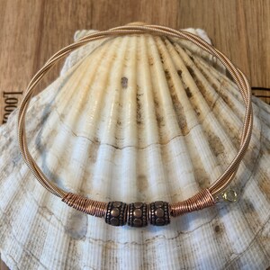 May include: A gold guitar string necklace with three copper beads. The beads have a textured design.