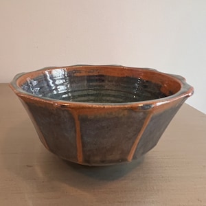 May include: A brown and gray ceramic bowl with a scalloped rim. The bowl has a glazed finish and a slightly irregular shape.