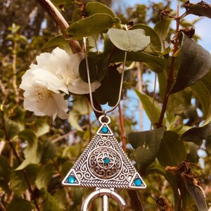 Puede incluir: Un collar de plata con un colgante triangular que presenta un dise&ntilde;o intrincado y piedras preciosas azules. El colgante tiene forma de llave con una cabeza circular y un tallo largo y delgado.