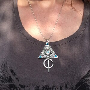 Puede incluir: Un collar de plata con un colgante triangular que presenta un dise&ntilde;o detallado con piedras preciosas turquesa. El colgante est&aacute; unido a una cadena de plata.