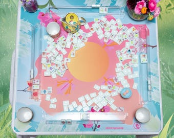 Puede incluir: Un juego de Mahjong con temática floral. El tablero rosa y azul presenta un círculo naranja. El juego incluye fichas, una tetera, tazas y flores en jarrones. El tablero está diseñado con un patrón floral.