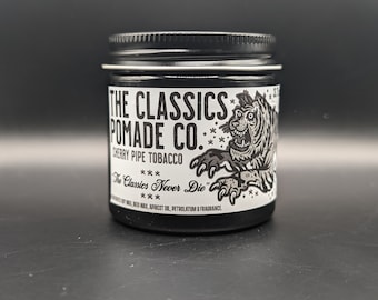 May include: A black jar of hair pomade with a white label that reads "The Classics Pomade Co." and "Cherry Pipe Tobacco". The label also features a black and white illustration of a tiger with the text "The Classics Never Die" underneath.